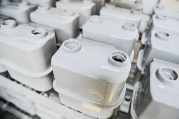 Rânduri de corpuri de contor de gaz vopsite în alb, stivuite laolaltă, fiecare cu două orificii filetate în partea de sus.