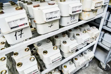 Stelaje cu contoare de gaz albe cu racorduri de alamă, unele numerotate de mână cu marker negru.