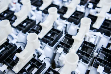 Rânduri de piese de contor de gaz din plastic alb, cu deschideri în formă de tub, deasupra unor carcase negre nervurate.