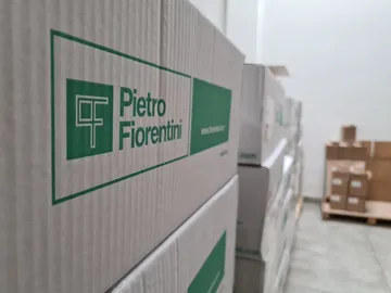 O cutie imprimată cu sigla verde Pietro Fiorentini, clar focalizată, cu stive de cutii estompate și un palet cu cutii maro în spate.