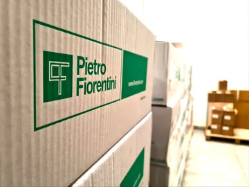 Cutii de carton stivuite, imprimate cu sigla verde Pietro Fiorentini, și alte cutii pe un palet în fundal.