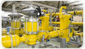 Conducte de gaz galbene, cu carcase rotunde de robinete și manometre, instalate într-o hală.
