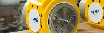 Două contoare de gaz galbene cu pistoane rotative, cu etichete FMG rotunde, albe, pe laterale, și un capac de oțel prins cu șuruburi în centrul celui din față.